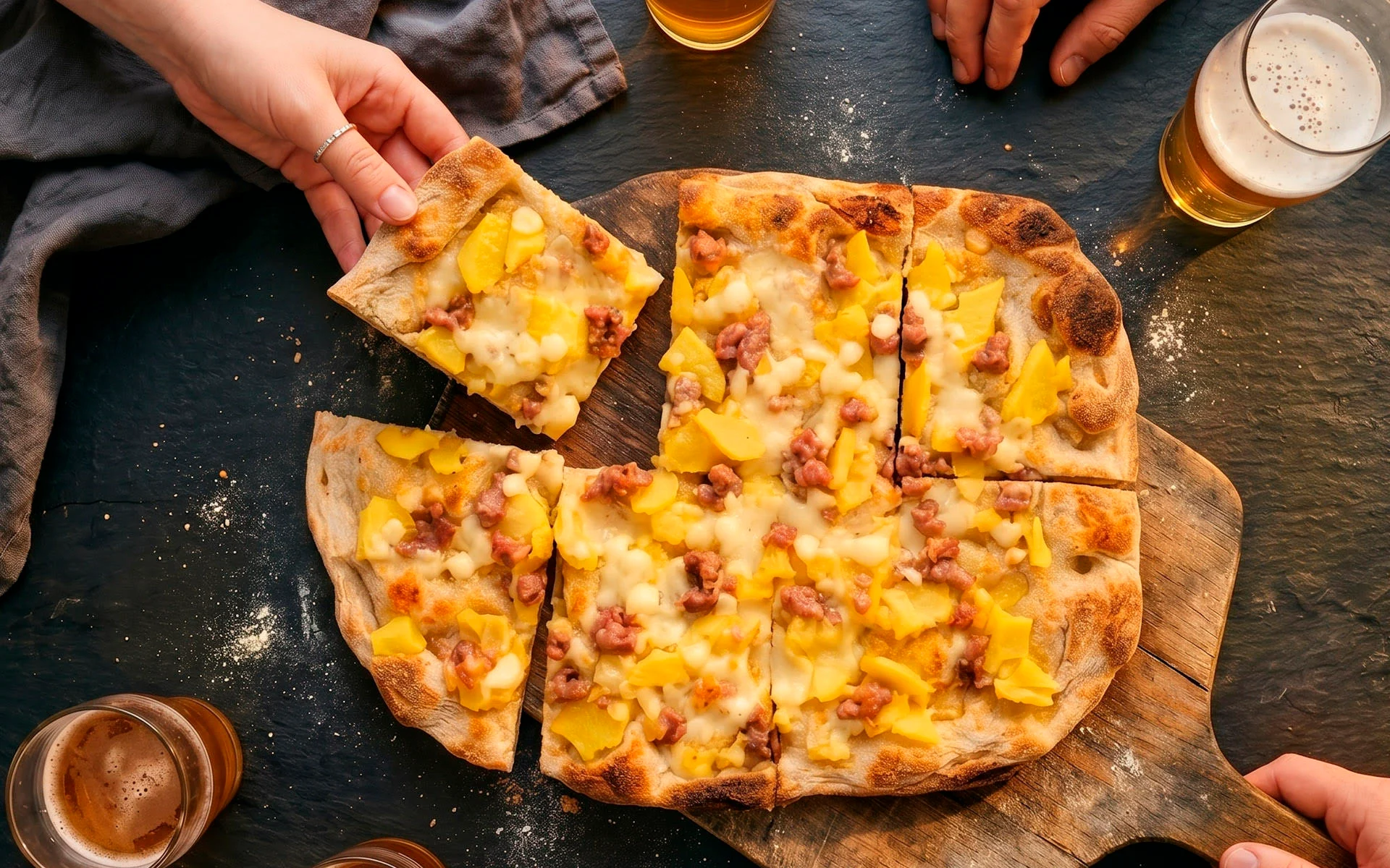 Une pinsa aux pommes de terre et à la saucisse est partagée à table